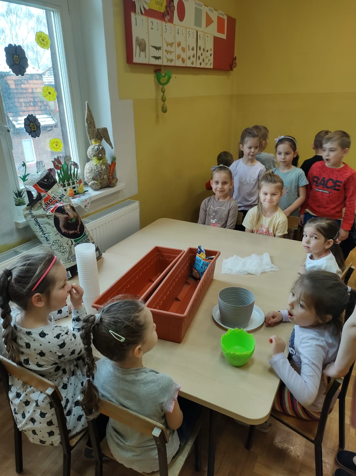 Dzieci stoją i siedzą dookoła stołu z nasionami